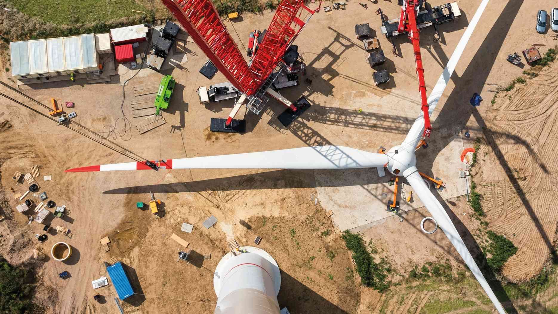 Baustelle einer Windenergieanlage mit Rotor und großen Montagekränen aus der Luft