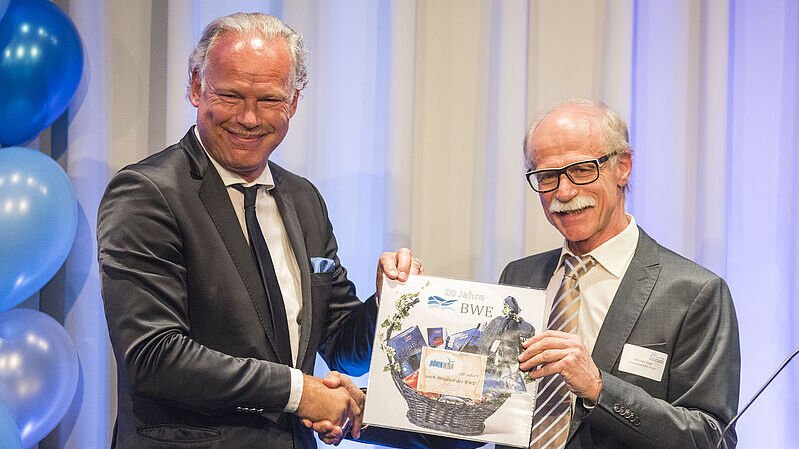 Hermann Albers zeigt mit einem älteren Herren ein Bild in die Kamera und dabei reichen sie sich die Hände