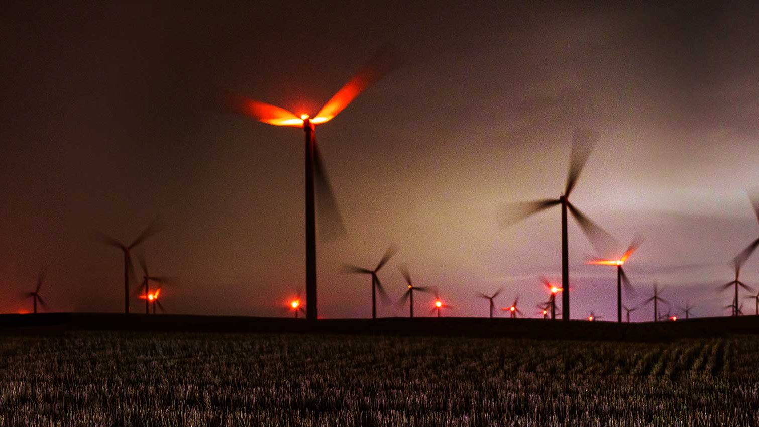 Windpark in der Dämmerung mit roten Hindernisfeuern unter dunklen Wolken