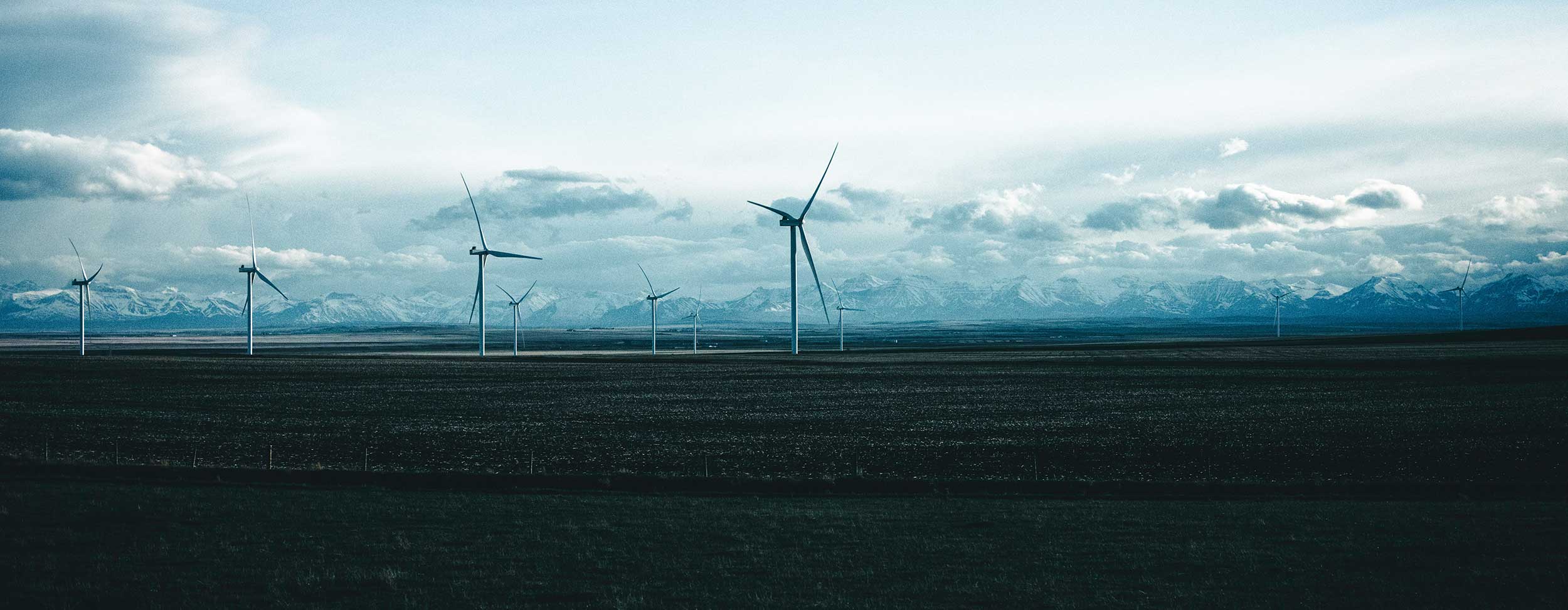 Windenergieanlagen in einer flachen Landschaft unter tiefen Wolken